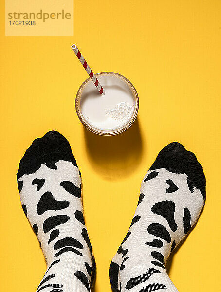 Fuß eines Mannes mit Socken mit Kuhmuster und einem Glas Milch auf gelbem Hintergrund