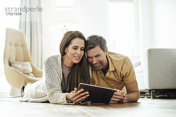 Lächelndes reifes Paar  das gemeinsam ein digitales Tablet benutzt  während es auf der Vorderseite einer Wohnung liegt