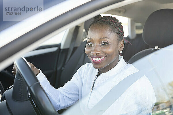 Lächelnde Frau hält das Lenkrad  während sie im Auto sitzt