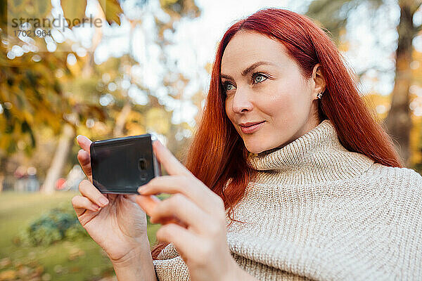 Nahaufnahme einer schönen Frau  die mit ihrem Mobiltelefon im Park fotografiert