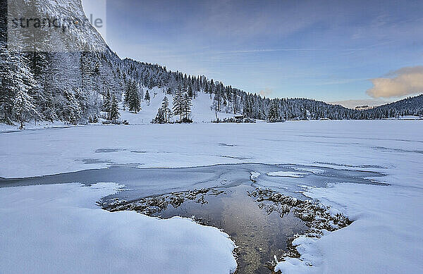 Bach inmitten von schneebedecktem Land zwischen Bergen und Himmel