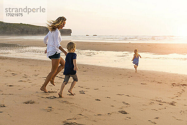 Mutter und Kinder genießen beim Laufen am Strand während des Sonnenuntergangs