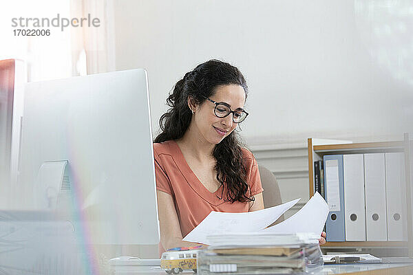 Lächelnde Geschäftsfrau  die ein Dokument liest  während sie in einer Bürokabine arbeitet