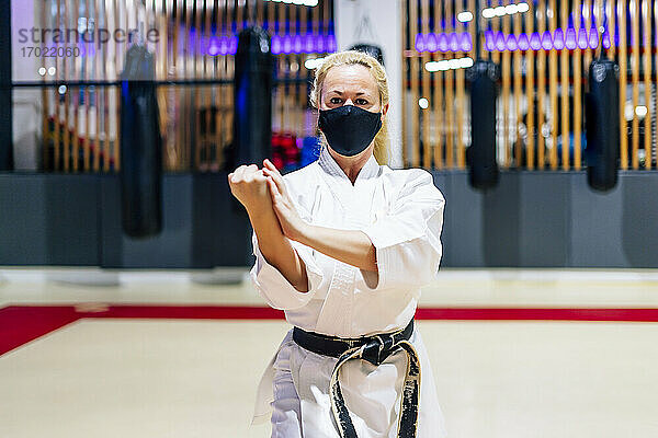 Ältere Frau mit Gesichtsmaske übt Karate im Fitnessstudio