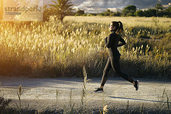 Junge Frau joggt auf dem Fußweg gegen die Landschaft bei Sonnenuntergang