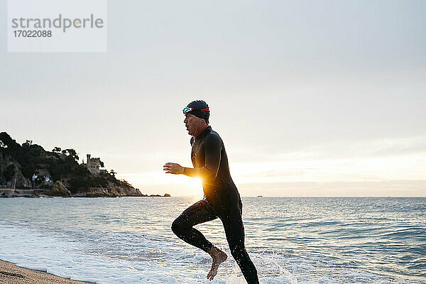 Männlicher Schwimmer verlässt das Wasser nach dem Schwimmen im Meer bei Sonnenuntergang