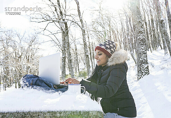Unternehmerin  die im Winter auf einer Bank sitzend am Laptop arbeitet