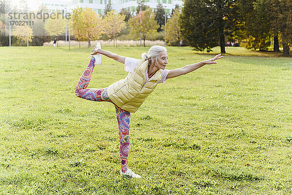 Ältere Frau macht Yoga-Übungen auf Gras in einem öffentlichen Park