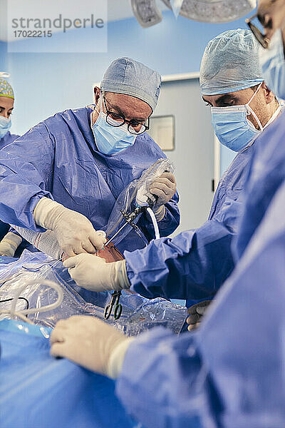 Älterer Arzt  der eine arthroskopische Operation an der Schulter mit einem Kollegen durchführt  während er im Operationssaal bei COVID-19 steht