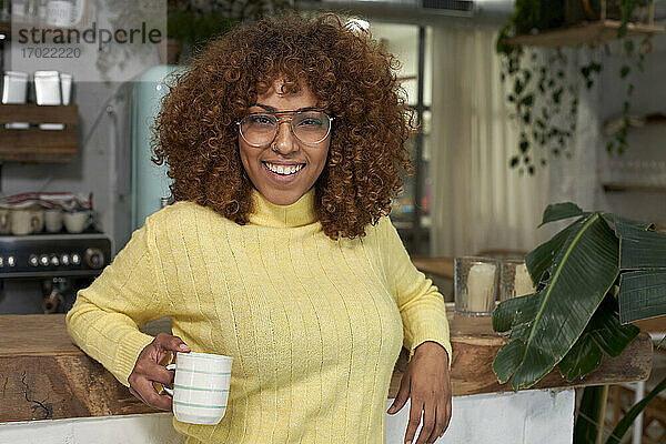 Lächelnde Frau mit Kaffeetasse an der Theke eines Cafés lehnend