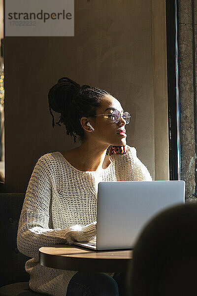 Junge nachdenkliche Frau  die mit ihrem Laptop in einem Café sitzt und wegschaut
