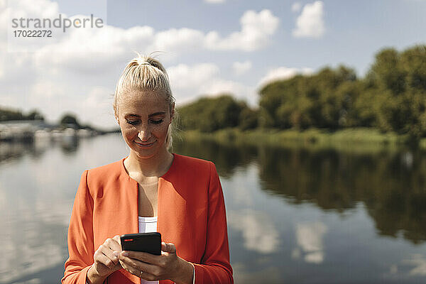 Eine Unternehmerin benutzt ihr Smartphone an einem sonnigen Tag am See