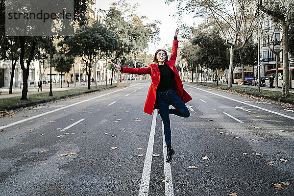 Junge Frau tanzt mit erhobenen Armen und springt auf die Straße