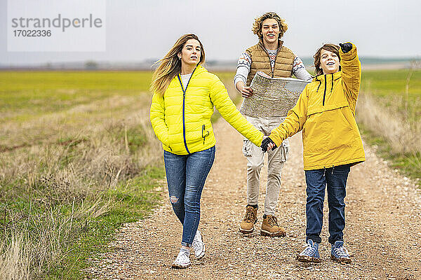 Drei Geschwister wandern mit Karte auf einem Feldweg
