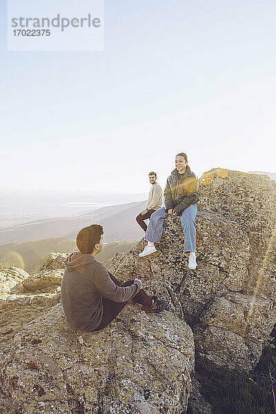 Freunde unterhalten sich auf dem Gipfel eines Berges bei klarem Himmel an einem sonnigen Tag