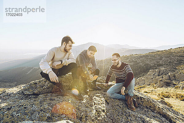 Männliche Freunde unterhalten sich im Sommer auf einem Berg vor einem klaren Himmel