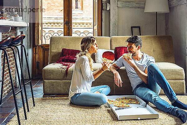 Junges Paar sitzt auf dem Boden des Wohnzimmers und isst Pizza aus einem Karton