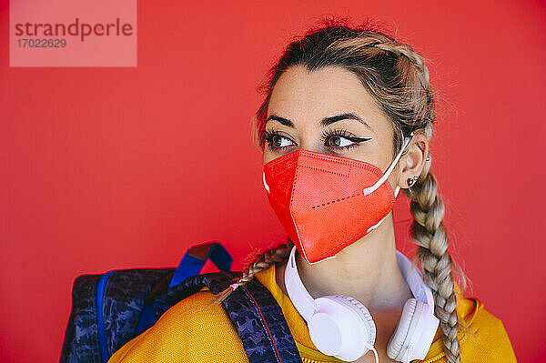 Junge Sportlerin mit Gesichtsschutzmaske  die wegschaut  während sie an einer roten Wand steht