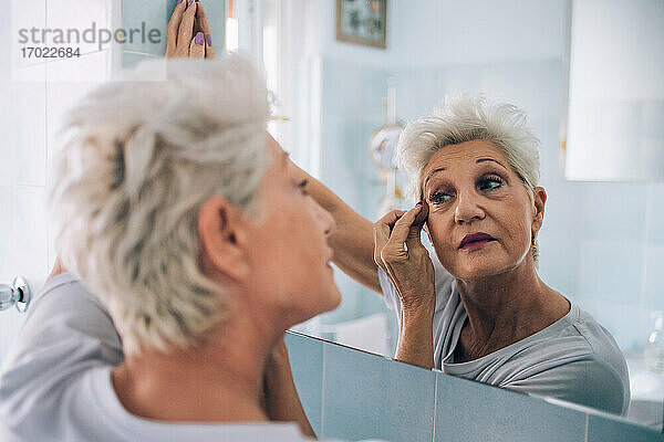 Ältere Frau schaut in den Spiegel  trägt Make-up auf