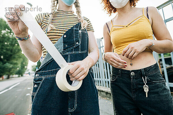 Junge Frauen mit Masken  die eine Rolle Klebeband halten