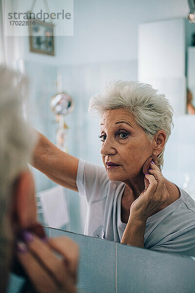 Ältere Frau schaut in den Spiegel  trägt Make-up auf