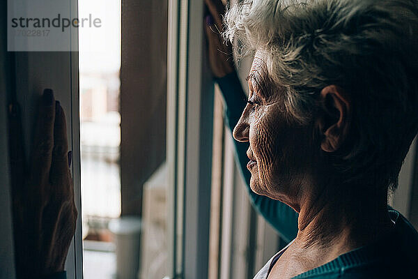 Ältere Frau schaut aus dem Fenster ihrer Wohnung