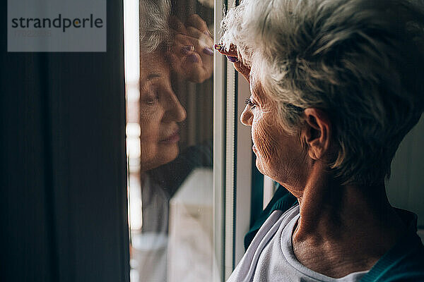 Ältere Frau schaut durch ein Wohnungsfenster