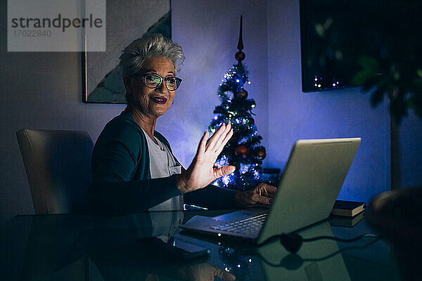 Frau winkt bei Videoanruf  Weihnachtsbaum im Hintergrund