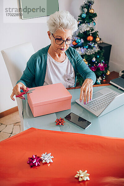 Frau verpackt Weihnachtsgeschenke Freigegeben (PR)esents  schaut auf ihr Handy