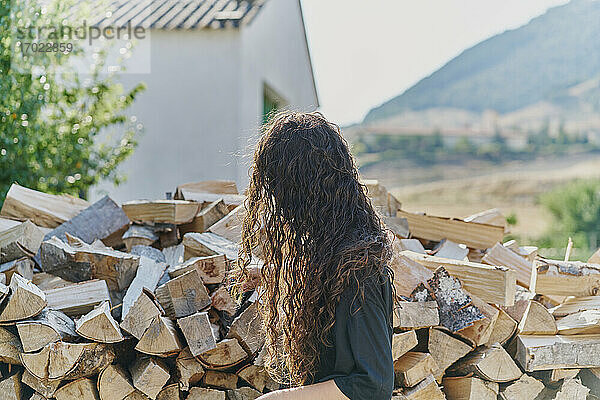 Junge Frau mit langen Haaren  an einem Holzstapel  Seitenansicht