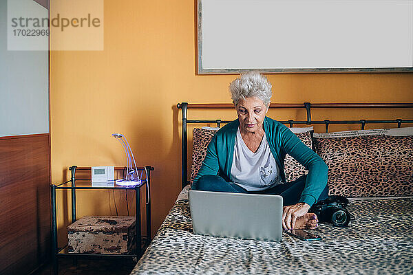 Fotograf auf dem Bett sitzend mit Laptop