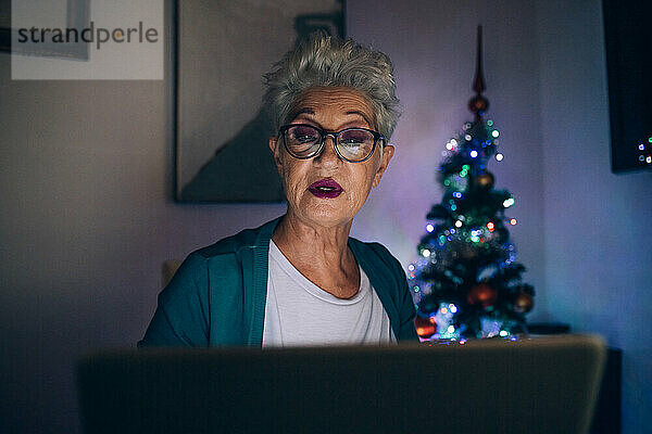 Frau benutzt Laptop bei Nacht  Weihnachtsbaum im Hintergrund