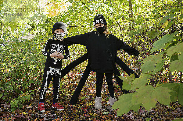 Mädchen (8-9) und Junge (6-7) tragen Halloween-Kostüme im Wald