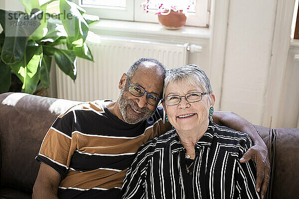 Lächelndes Paar mit Arm um sitzen auf Sofa zu Hause