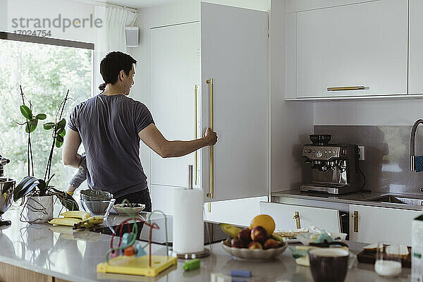 Vater öffnet Kühlschrank  während er seinen kleinen Sohn in der Küche trägt