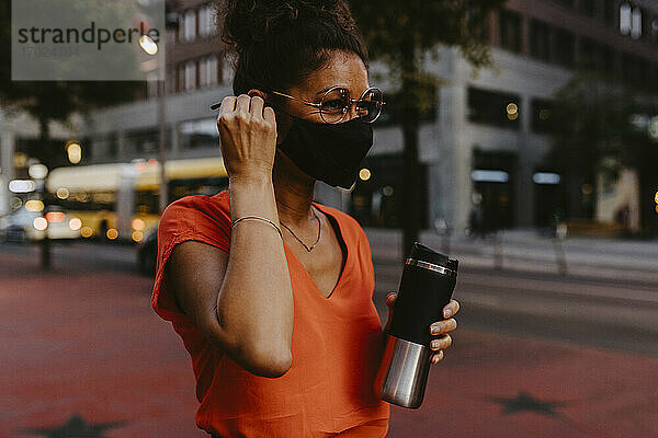 Geschäftsfrau mit Gesichtsschutzmaske und Isolierbehälter in der Stadt