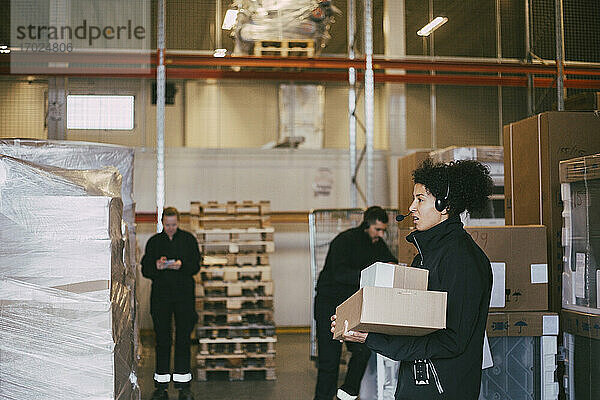 Unternehmerin hält Pakete und steht neben Kollegen im Logistiklager