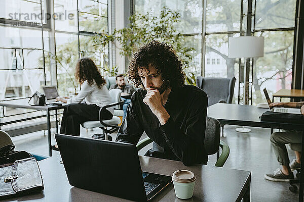 Männlicher Unternehmer bei der Arbeit am Laptop im Coworking-Büro nachdenklich