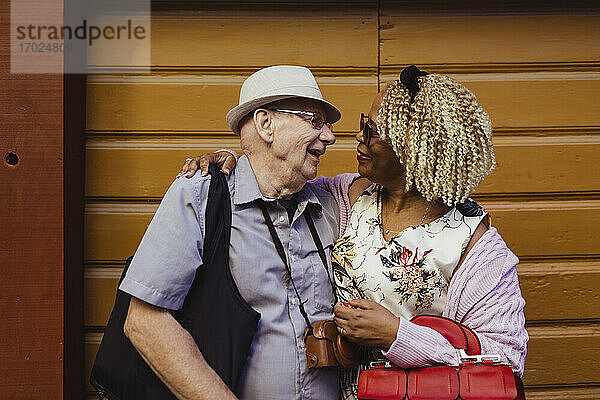 Lächelnde Senior Paar mit Armen um gegen die Wand