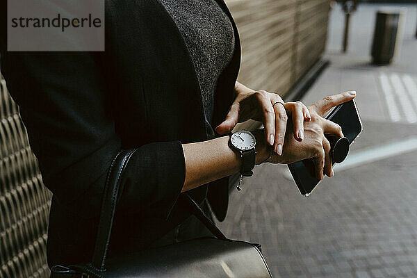 Mittelteil einer Geschäftsfrau  die die Zeit auf der Armbanduhr überprüft