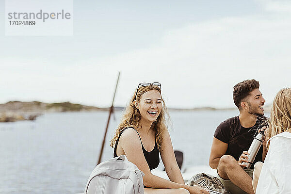 Junge Freunde lachen  während sie Picknick gegen Meer und Himmel genießen