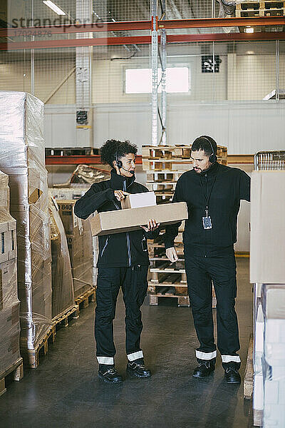 Weibliche Unternehmerin hält Pakete  während sie sich mit einem männlichen Kollegen im Logistiklager unterhält