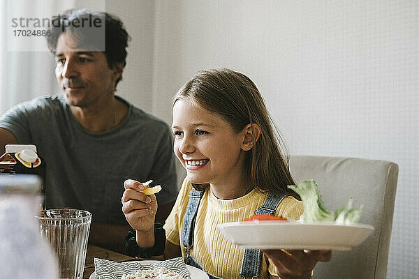 Tochter isst Frühstück sitzend bei Vater zu Hause