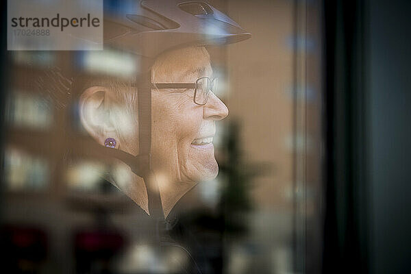 Lächelnde Seniorin durch Fenster zu Hause gesehen