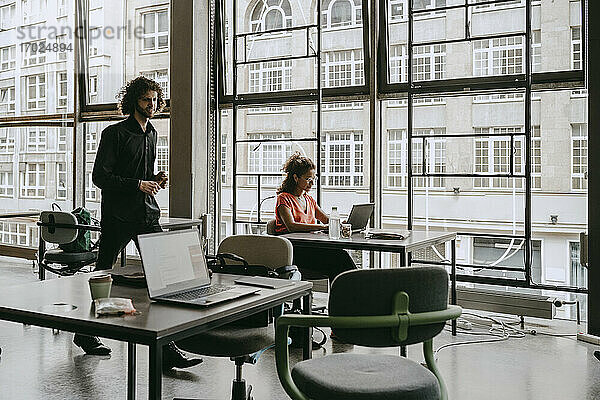 Weibliche Unternehmerin benutzt Laptop  während ein männlicher Kollege im Coworking Space vorbeigeht