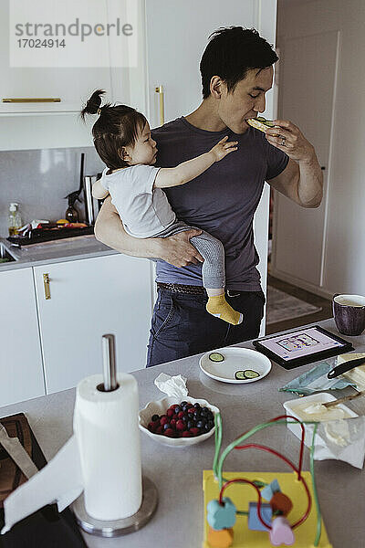 Vater isst Essen  während Baby Sohn schaut ihn in der Küche zu Hause
