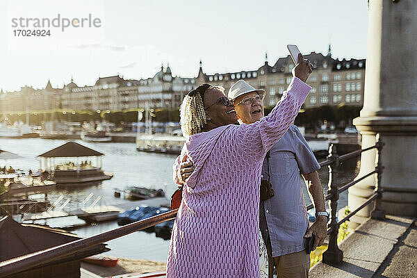 Lächelnde ältere Paar unter selfie während stehend auf Brücke gegen See in der Stadt