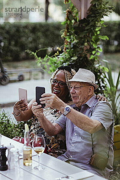 Fröhliche ältere Paar unter Selfie auf Smartphone beim Sitzen in Bürgersteig Café