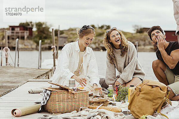 Freunde lachen beim Snacken während eines Picknicks am Hafen