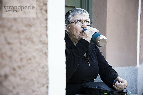 Durstige Frau trinkt Wasser aus einer Flasche am Eingang